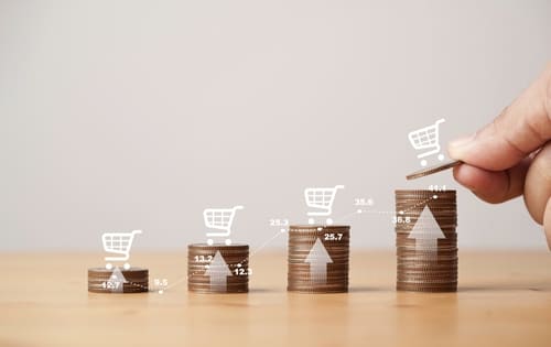 Stacked coins with shopping cart icons showing growth, representing ecommerce trends in online sales.